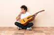 © luismolinero - Young caucasian man with a guitar sitting on the floor thinking an idea and looking side