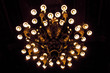 Antigua araña estilo europeo neoclásico iluminada con todas sus luces encendidas sobre fondo negro.