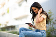© mimagephotos - smiling young woman sitting outside looking at mobile phone