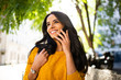 © mimagephotos - Close up smiling young brunette woman walking and talking with cellphone in city