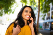© mimagephotos - Close up smiling young hispanic woman walking and talking with cellphone in city