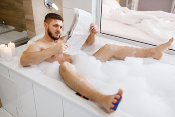 Man reads newspaper in bath with foam