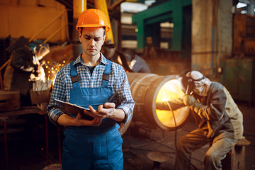 Master with notebook and welder on factory