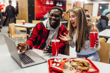 Stylish and positive friends sits in a cafe eating yummy fast food with cola. Spending time together, having fun.