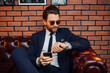 © Тарас Нагирняк - Attractive bearded man wearing  suit sitting on the leather sofa holding smartphone. Comfort and relaxation.