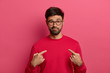 © WHstudio Leushin N - I can handle it. Assertive determined man with beard points at himeself, feels proud and brags about own achievements, proposes own help, wears red sweater, eyewear, stands against pink background