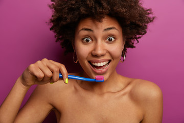 Wall Mural - Brush your teeth every morning. Naked curly woman holds toothbrush near mouth, cares about personal hygiene, has healthy habits, enjoys freshness and cleanliness after cleaning teeth, stands indoor