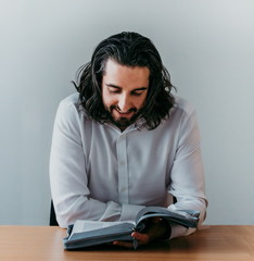 High angle shot of a man reading his Bible while sitting inside - Young student of bible contemplating and reading Bible - Long hair spiritual person studying and reading God's word holy scriptures