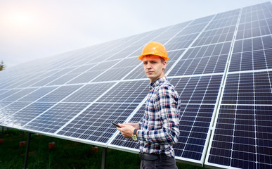 Wall Mural - Male engineer in helmet with tablet in hands standing near solar panels. Concept ecology protection.