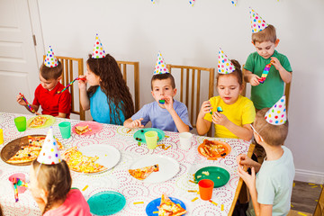 Lovely children wearing birthday hats having fun together. Kids eating tasty pizza at party