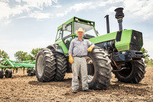 Farmer Leaning On Wheel Of A Tractor In A Plowed Field. Bridger, Montana, USA