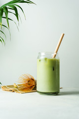 Making Japanese iced matcha latte, green tea with milk, soy milk, traditional matcha tools, with bamboo straw in glass on white background.