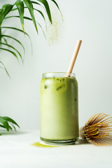 Making Japanese iced matcha latte, green tea with milk, soy milk, traditional matcha tools, with bamboo straw in glass on white background.