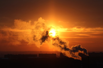 Wall Mural - red sun at sunset or dawn at dusk low above the horizon shrouded in smoke from the chimneys of the p