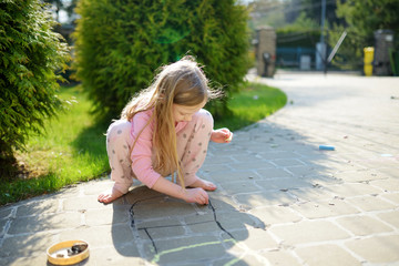 cute little girl drawing with colorful chalks on a sidewalk. summer activity for small kids.