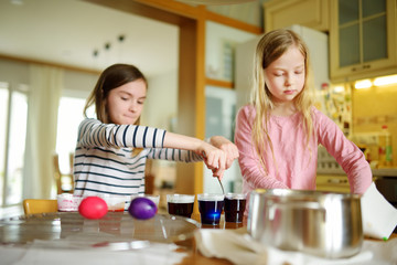 Wall Mural - Two cute young sisters dyeing Easter eggs at home. Children painting colorful eggs for Easter hunt. Kids getting ready for Easter celebration.