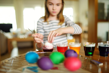 Wall Mural - Cute young girl dyeing Easter eggs at home. Child painting colorful eggs for Easter hunt. Kid getting ready for Easter celebration.