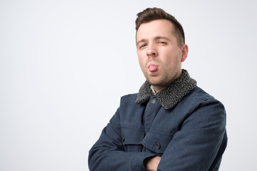 Sticker - Young man in warm jeans jacket showing tongue looking jokingly and playfully.