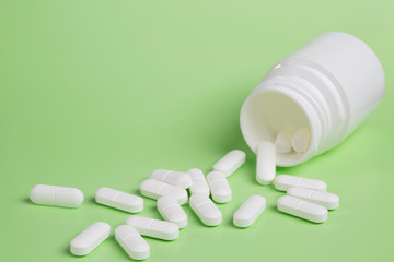 Wall Mural - Plastic white bottles of pills on a green background of scattered white pills