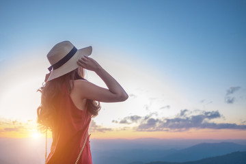 Smiling woman traveler in mountains at sunset holding hat and looking at view of nature chiangmai landmark in thailand with backpack in holiday, relaxation concept, travel concept