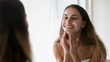 © fizkes - Smiling young woman scrub face with beauty mask