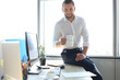 © ty - Good looking young business man drinking coffee and smiling while sitting in the office.