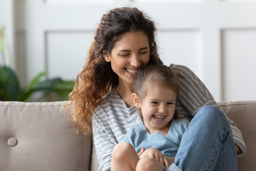 Wall Mural - Laughing curly mom embracing little child girl.