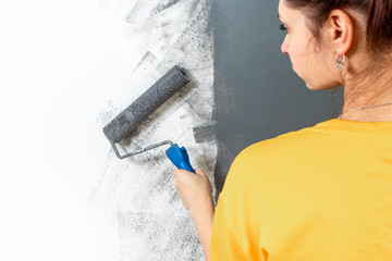 Beautiful young girl paints a wall in a yellow jacket with a roller, gray paint. The concept of repair, change, design, interior.