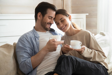 Wall Mural - Loving young couple hug on couch drinking tea