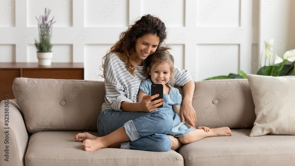 Happy pretty mommy cuddling small daughter, taking selfie on cellphone. - obrazy, fototapety, plakaty 