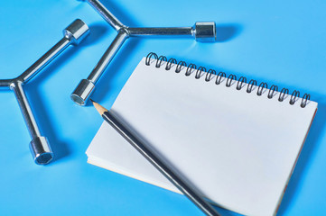 Wall Mural - Two glossy chrome wrenches for nuts lies near blank paper notebook and black pencil on blue desk in workshop. Space for text