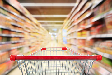 Wall Mural - Empty red shopping cart with supermarket aisle interior with product shelves abstract blur background