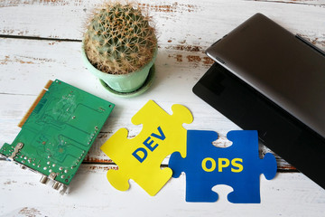 puzzle with Dev and Ops words near laptop and motherboard. DevOps Concept for software engineering culture and practice of software development and operation