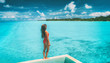 Beach summer luxury travel vacation resort swimsuit woman standing on infinity pool looking at blue turquoise crystalline ocean landscape of South Pacific private island, Tahiti, French Polynesia.