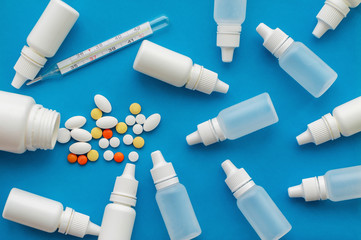 Texture. A jar of pills, thermometers and nasal drops on a blue background. The view from the top. Concept of health protection.