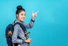Happy Asian Woman Travel Backpacker Standing Pointing Hands To Copyspace On Blue Background. Cute Asia Girl Smiling Wearing Casual Jeans Shirt And Finger Pointing To Aside For Present Promotions.