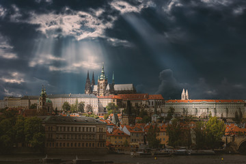 Prague City in Czech Republic with St Vitus Cathedral and Historical Buildings in Sunlight. Houses and Vltava River with Charles Bridge Before Storm. Heavy Clouds on Sky.