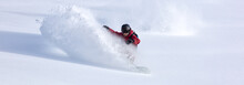 Heliski Snowboarding. Freerider In A Bright Suit Rides Snowboarding With Large Splashes Of Snow On A Sunny Day. Young Snowboarder. Concept Snowboard. Big Swirls Of Fresh Snow In Good Powder Day