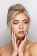© spritnyuk - A large head portrait of a beautiful young girl with dyed blonde hair arranged in a hairstyle, with makeup and beautiful lips and teeth. Hands near the face. a neutral gray background