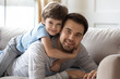 © fizkes - Carefree boy cuddling smiling dad, looking at camera.