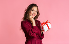 Pretty young woman holding gift box and looking at camera