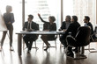 © fizkes - Smiling black businesswoman raising hand asking female lead in boardroom.