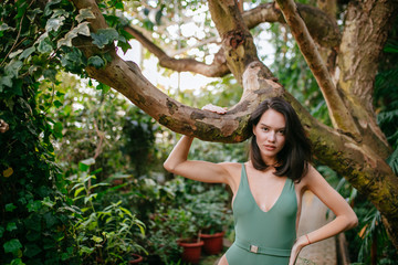 Wall Mural - caucasian brunette woman in wild tropical rainforest, wearing green stylish bikini or swimsuit. lady look at camera, beautiful good-looking face and slim body. lifestyle, people connected with nature