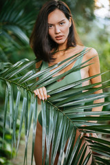 Wall Mural - caucasian brunette woman in wild tropical rainforest, wearing green stylish bikini or swimsuit. lady look at camera, beautiful good-looking face and slim body. lifestyle, people connected with nature