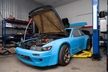 Poster - A powerful tuned blue sports car with an open hood and a powerful engine stands on a lift in a workshop for repair and maintenance of vehicles. Auto service industry and tuning.