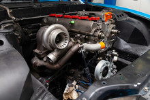 Powerful Tuned Gasoline Engine With A Turbocharger And A Charger In The Engine Compartment Of An Automobile With An Open Hood And A Turbine In A Car Repair And Improvement Workshop.