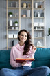 © BestForYou - Attractive young woman is reading a book, looking at camera and smiling sitting on a cozy sofa