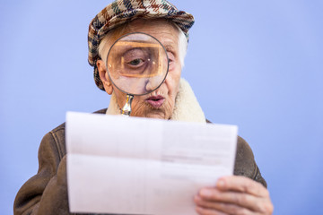 Wall Mural - Funny portraits with old grandmother. Senior woman acting as an investigator with the magnifying lense