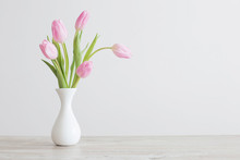 Pink Tulips In White Ceramic Vase On Wooden Table On Background White Wall