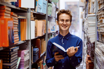 Happy male student standing in library with book, reading interesting detective story